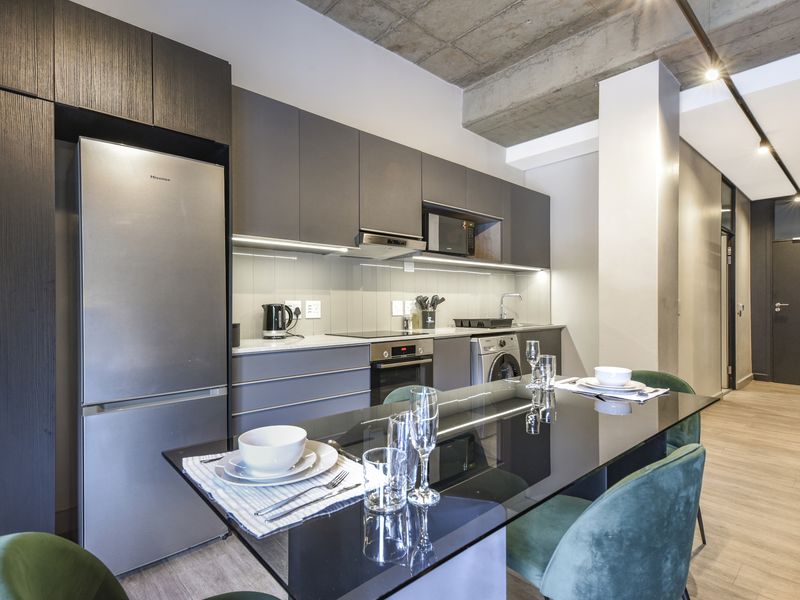 Modern open-plan kitchen featuring sleek cabinetry, integrated appliances, and an exposed concrete ceiling, seamlessly flowing into the dining area.