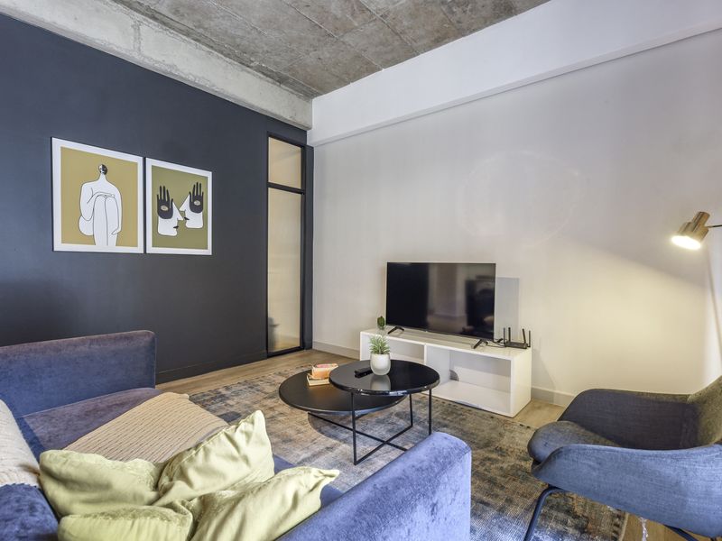 Modern living room featuring an exposed concrete ceiling, a dark accent wall, and neutral flooring, creating a contemporary urban aesthetic.