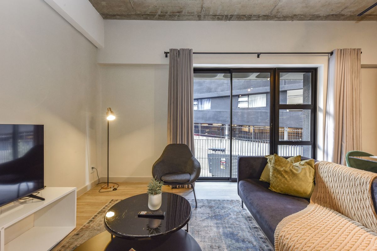 Modern living room featuring an exposed concrete ceiling, laminate flooring, and large sliding glass doors providing access to the exterior.