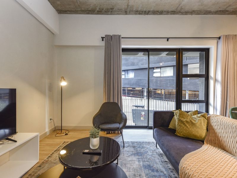 Modern living room featuring an exposed concrete ceiling, laminate flooring, and large sliding glass doors providing access to the exterior.