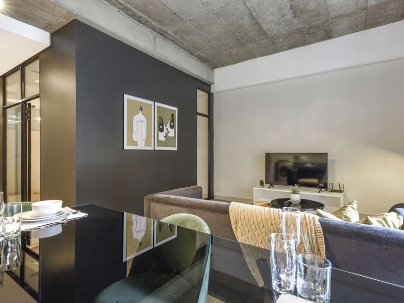 Modern open-plan living area featuring an exposed concrete ceiling, striking black accent wall, and contemporary glass partitions for a sleek, industrial aesthetic.