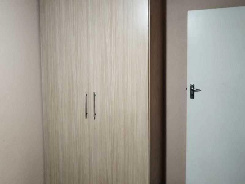 A bedroom featuring a light wood-finish built-in wardrobe with modern handles.