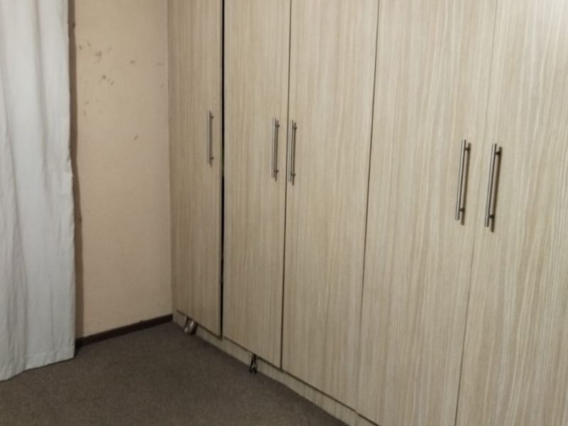 A bedroom featuring built-in wooden cupboards, neutral wall paint, and carpeted flooring.