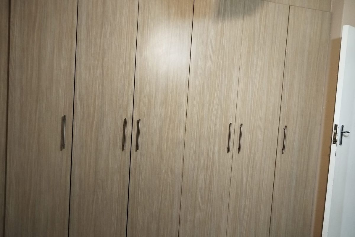 A bedroom featuring floor-to-ceiling built-in cupboards with a light wood-grain finish and modern metal handles.