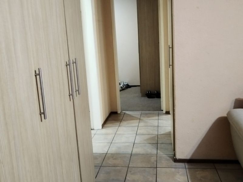 A functional hallway featuring light wood-finish built-in cupboards and neutral floor tiles, providing access to adjacent rooms.