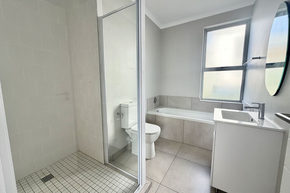 A clean, modern bathroom featuring a glass-enclosed shower, a built-in bathtub, a vanity basin, and a toilet with neutral floor and wall tiling.