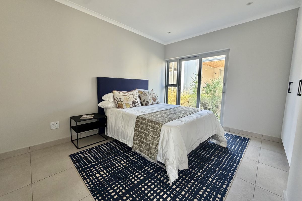 A bright bedroom featuring neutral tiled flooring, built-in cupboards, and a sliding glass door providing direct access to the outdoor area.
