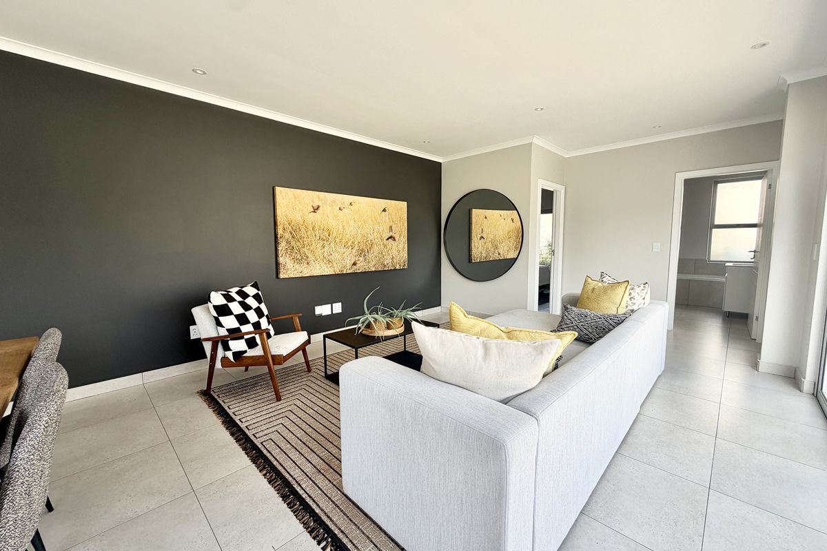 A modern, well-maintained living room featuring neutral tiled flooring, a striking dark accent wall, and recessed downlighting.