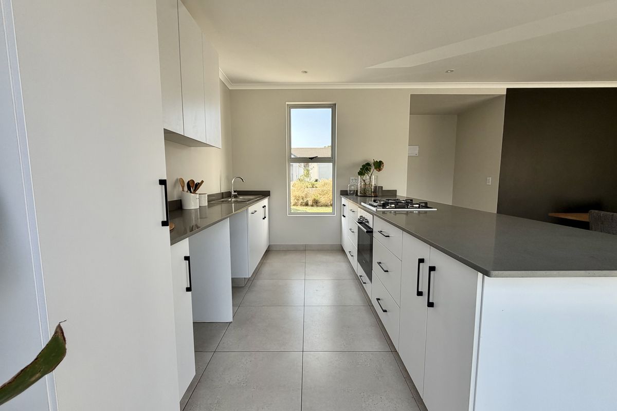 Modern kitchen featuring white cabinetry, stone countertops, a gas hob, built-in oven, and tiled flooring in a clean, minimalist layout.