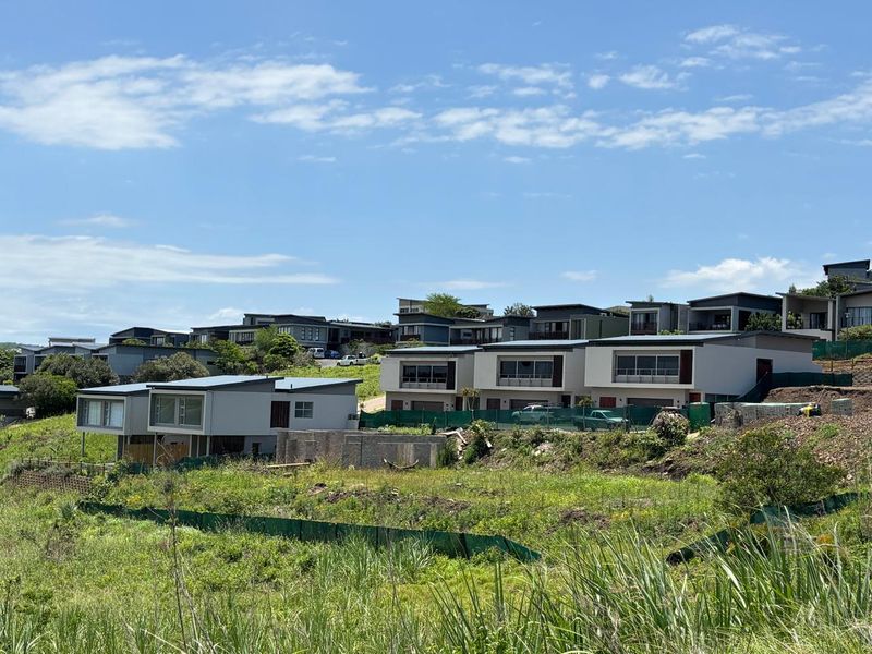 A view of a modern residential estate featuring contemporary homes with pitched roofs and balconies, set against a backdrop of undeveloped land.