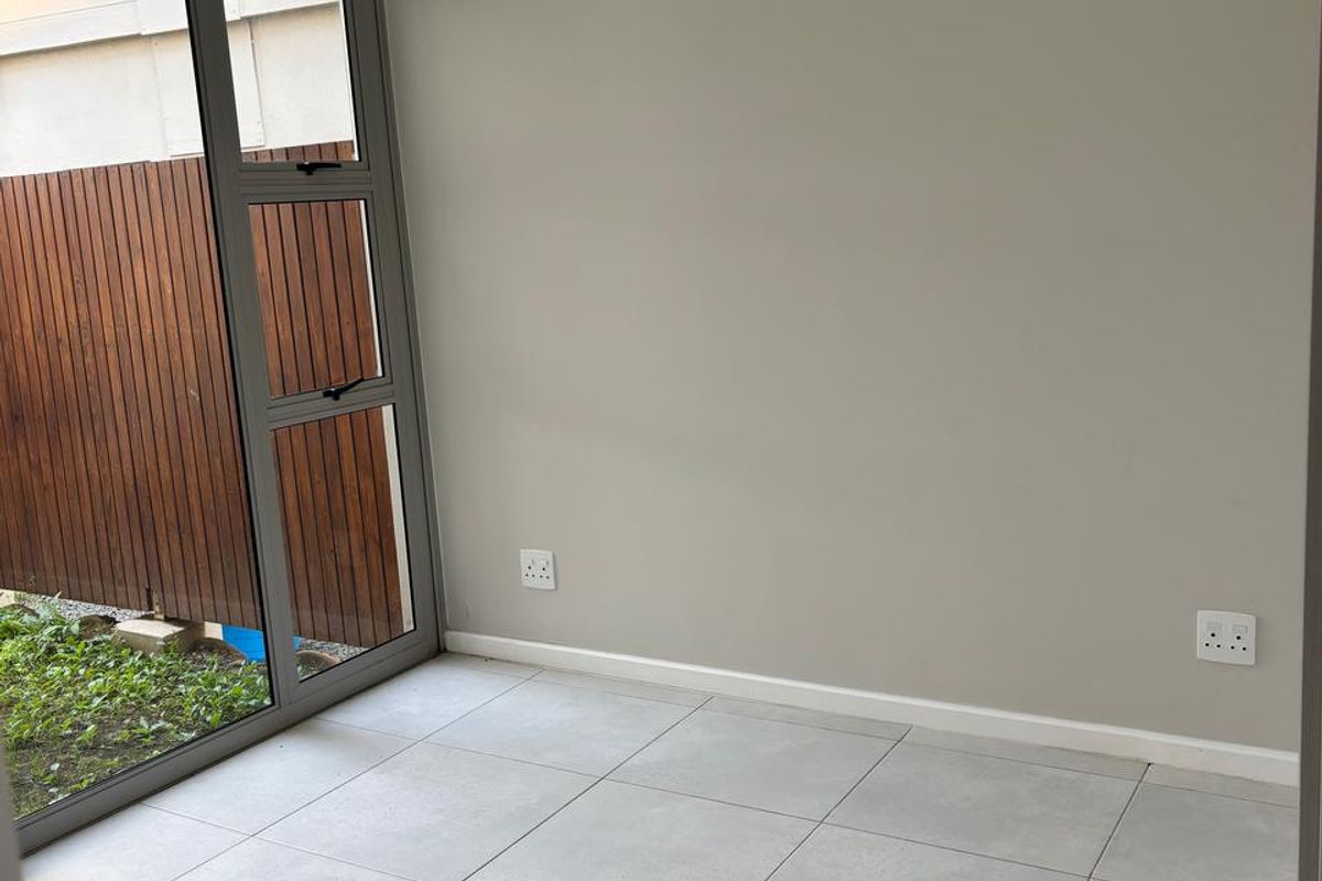 A bright, empty living space featuring neutral tiled flooring, modern grey aluminium sliding doors, and clean painted walls with integrated power outlets.