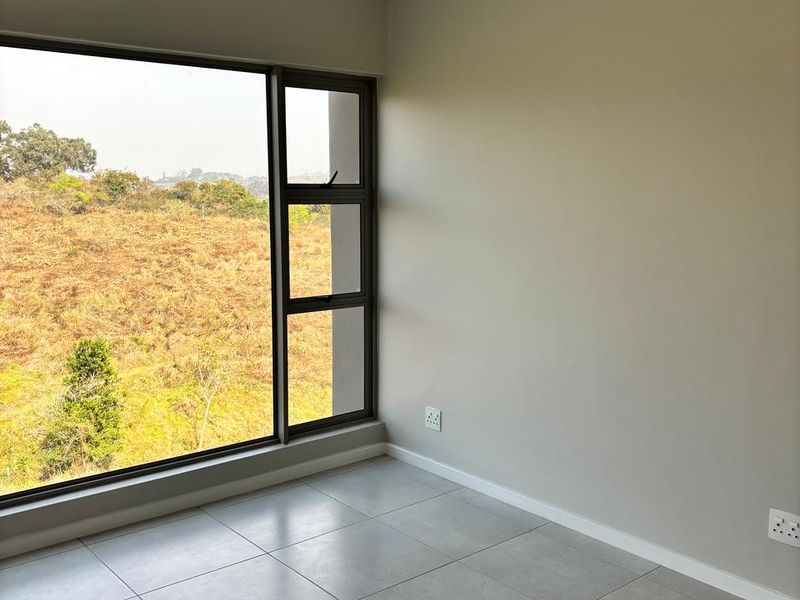 A bright, modern, and empty bedroom featuring large aluminium windows with scenic views, neutral tiled flooring, and a ceiling fan.