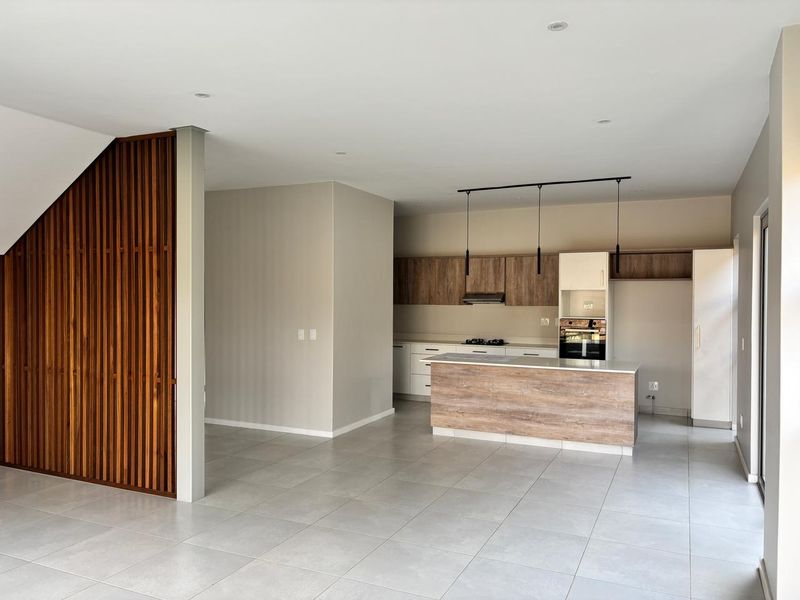 Modern open-plan kitchen featuring a central island, built-in appliances, and a decorative timber slat feature wall, finished with neutral tones and tiled flooring.