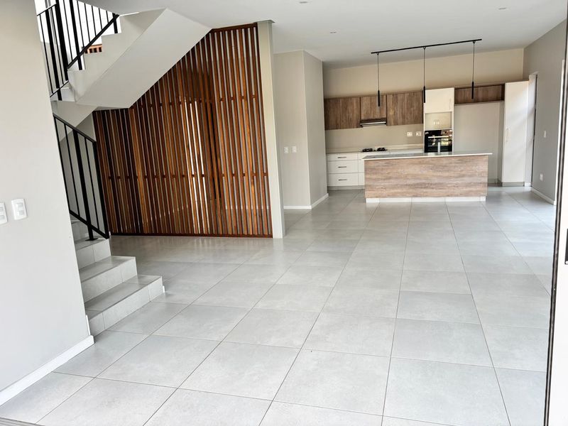 Spacious open-plan living area featuring modern tiled floors, a striking wooden slat partition, and a contemporary kitchen with built-in cabinetry and island.
