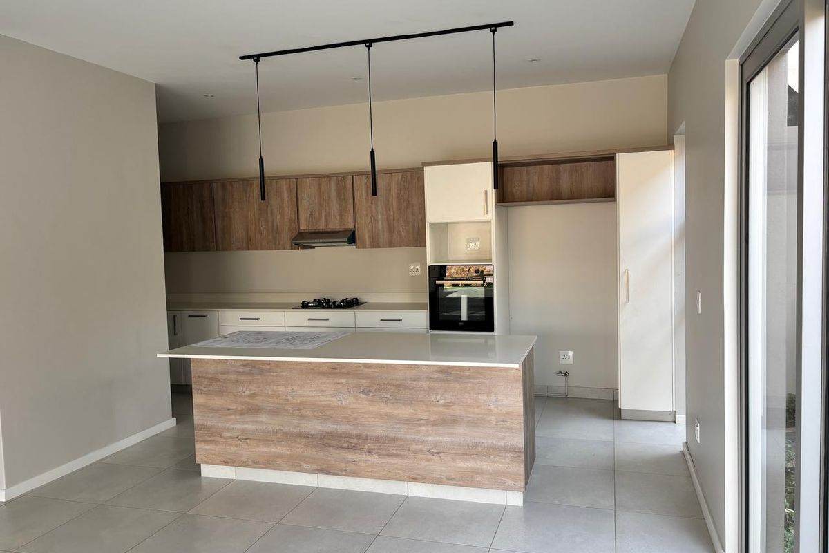 Modern kitchen featuring a central island, built-in oven, gas hob, extractor fan, and sleek laminate cabinetry with stone countertops.