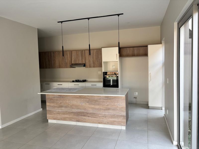 Modern kitchen featuring a central island, built-in oven, gas hob, extractor fan, and sleek laminate cabinetry with stone countertops.