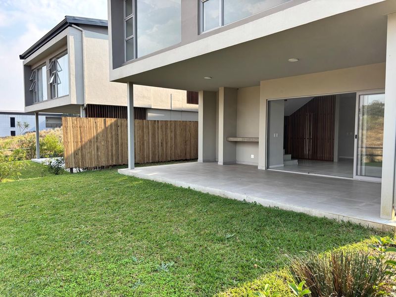A modern covered patio featuring tiled flooring, recessed lighting, and a built-in concrete counter, seamlessly connecting to the interior living space and rear garden.