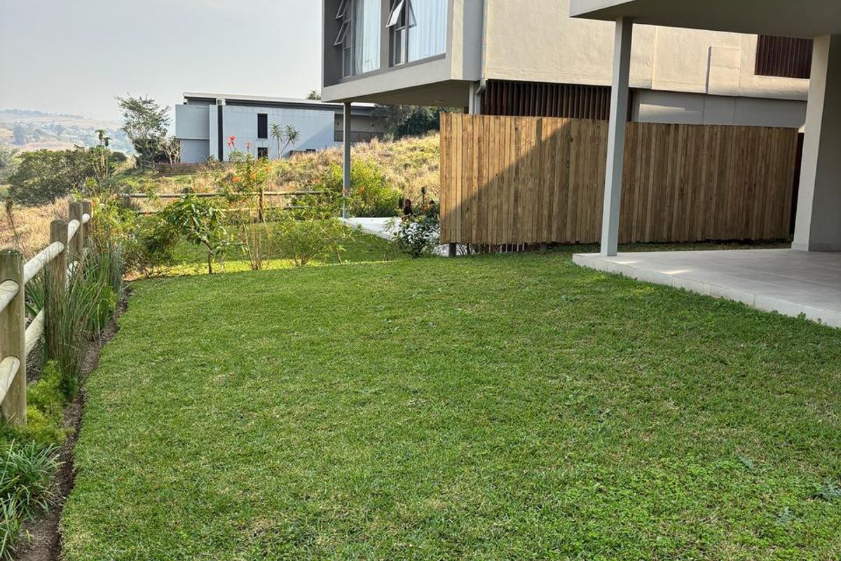 A well-maintained rear garden featuring a manicured lawn, timber fencing, and a covered concrete patio area with views of the surrounding landscape.