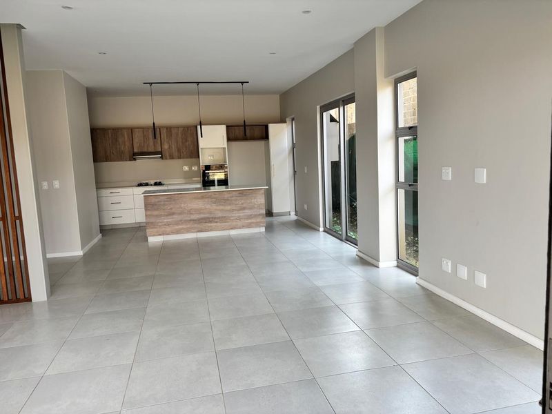 Spacious open-plan living and kitchen area featuring modern cabinetry, a central island, tiled flooring, and large sliding doors leading to the exterior.