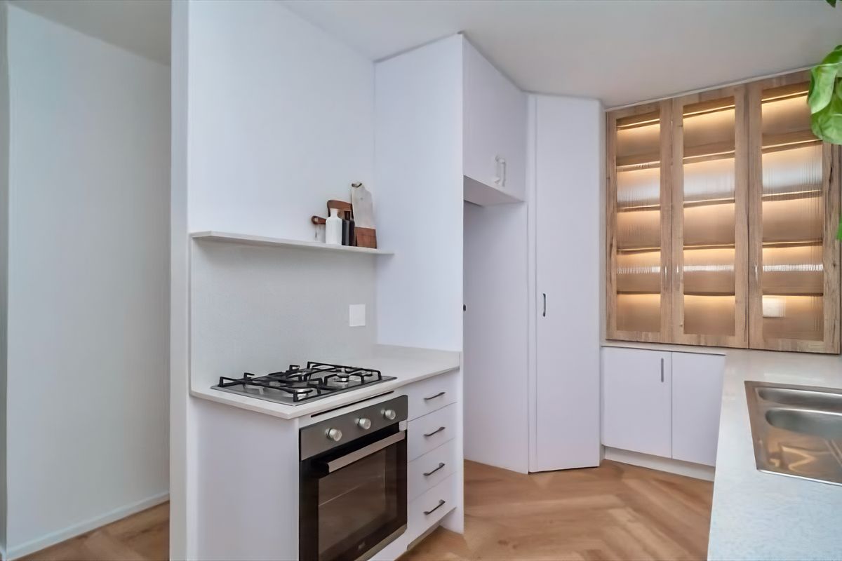 Modern kitchen featuring white cabinetry, gas hob, built-in oven, stone countertops, and elegant herringbone timber flooring with integrated display lighting.