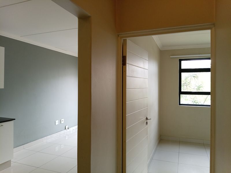 A bright, empty hallway connecting to adjacent living and bedroom spaces, featuring neutral wall tones and clean tiled flooring throughout.