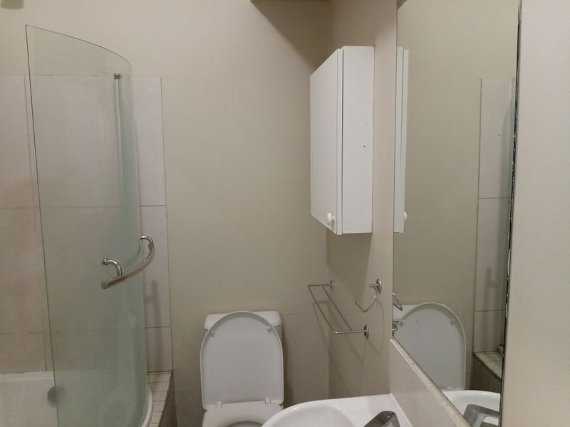 A functional bathroom featuring a shower with a glass screen, a toilet, a wall-mounted cabinet, and a vanity mirror.