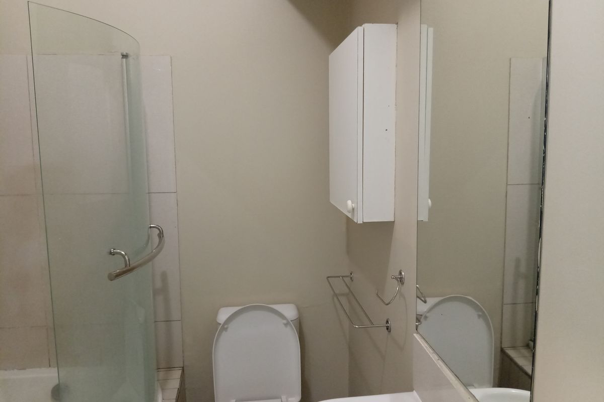 A functional bathroom featuring a shower with a glass screen, a toilet, a wall-mounted cabinet, and a vanity mirror.