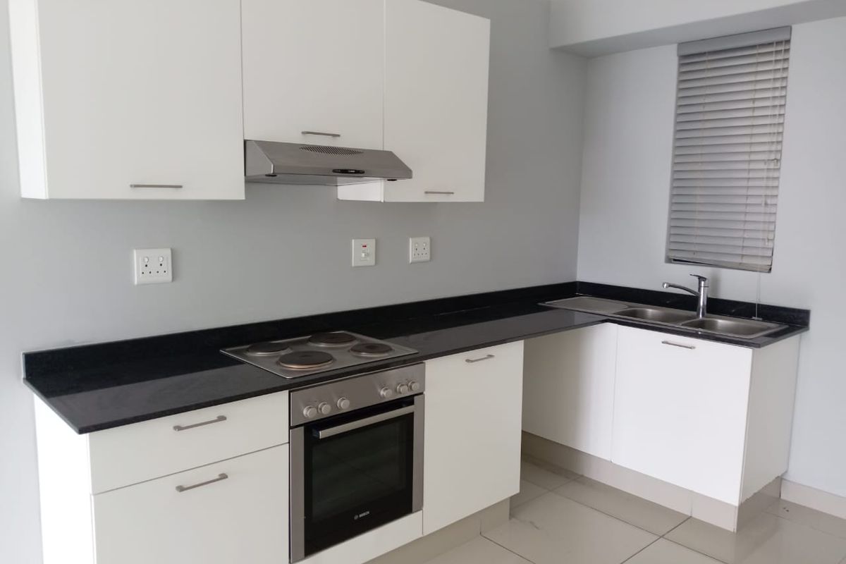 Modern kitchen featuring white cabinetry, black granite countertops, built-in oven, electric hob, extractor fan, and a double sink with tiled flooring.