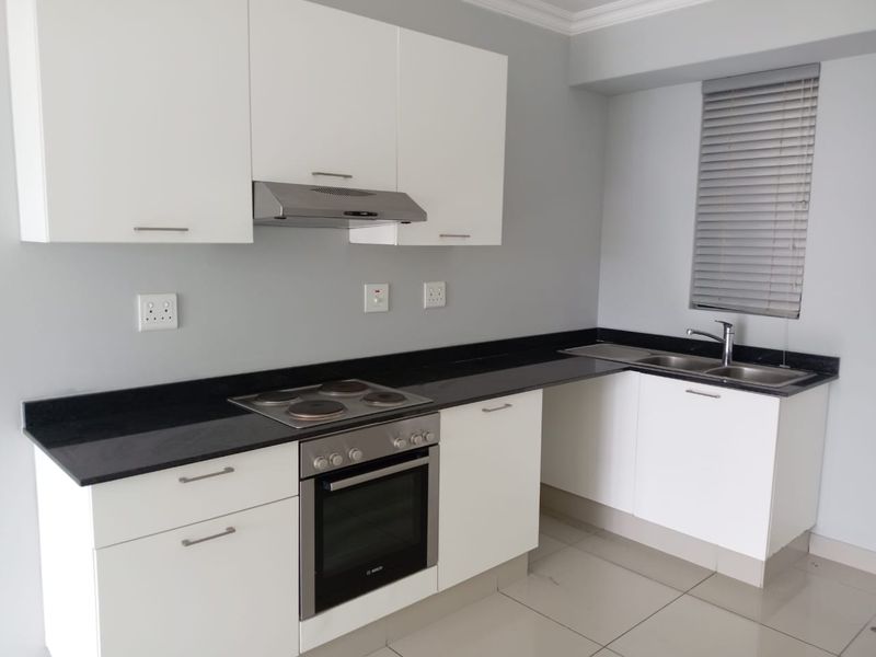 Modern kitchen featuring white cabinetry, black granite countertops, built-in oven, electric hob, extractor fan, and a double sink with tiled flooring.