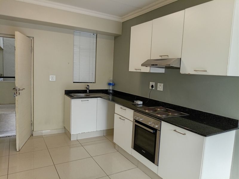 A functional kitchen featuring white cabinetry, granite countertops, built-in oven, electric hob, and tiled flooring, offering a clean and practical workspace.