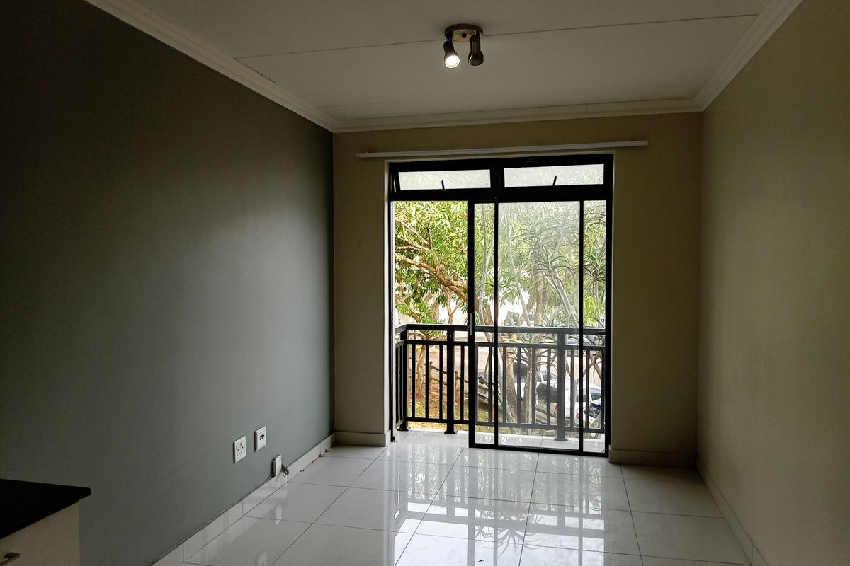 An empty living room featuring polished tiled flooring, a neutral color palette, and a sliding glass door providing access to a private balcony.