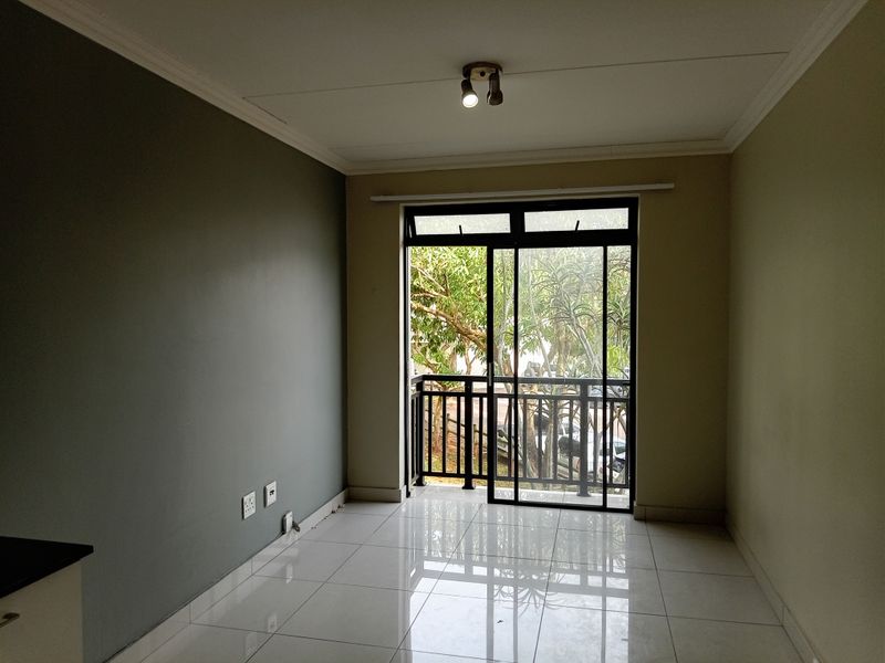 An empty living room featuring polished tiled flooring, a neutral color palette, and a sliding glass door providing access to a private balcony.