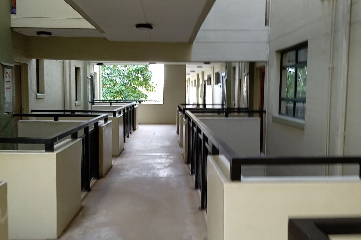 An open-air apartment complex hallway featuring concrete flooring, metal safety railings, and recessed lighting, providing access to residential units.