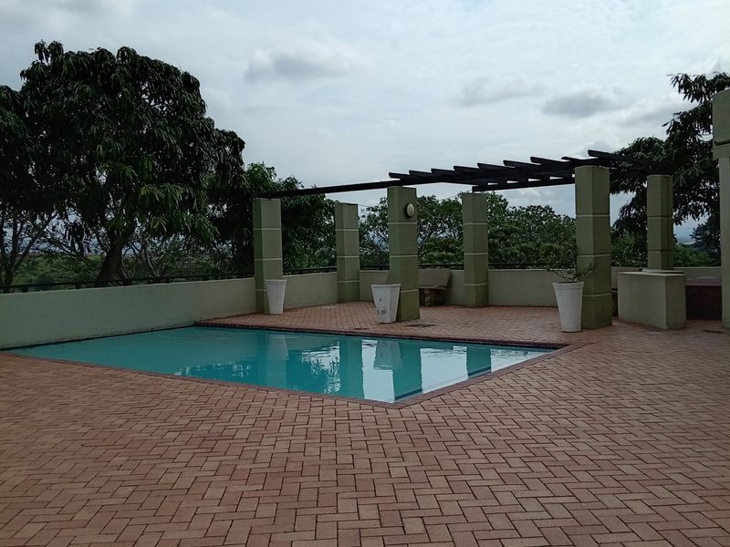 An outdoor pool area featuring a swimming pool, brick paved deck, and a pergola structure with concrete pillars.