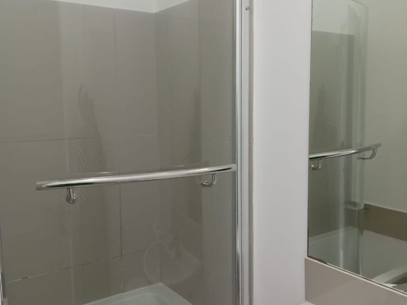 A clean, functional bathroom featuring a curved glass shower enclosure, wall-mounted basin with mixer tap, and a large vanity mirror.