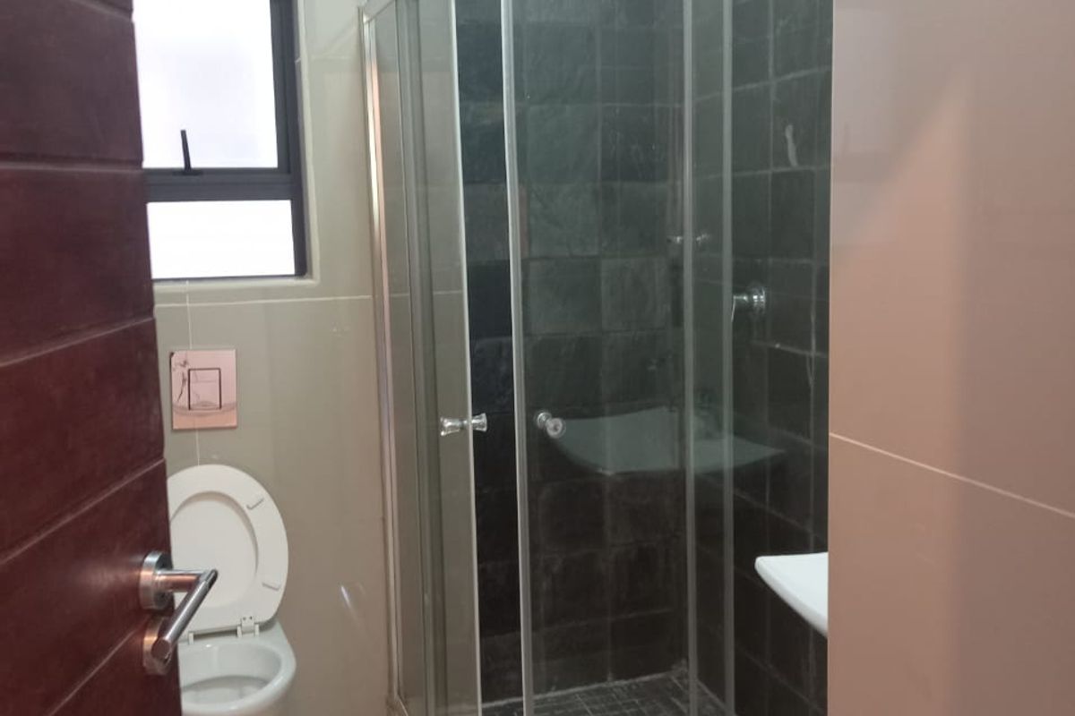 A clean, modern bathroom featuring a glass shower enclosure, wall-mounted toilet, and contrasting dark tiled shower wall.