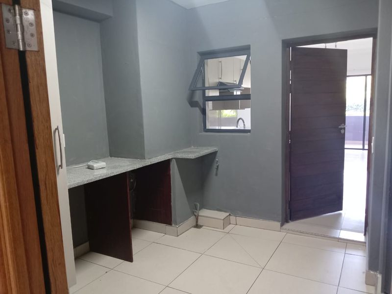 A functional laundry area featuring tiled flooring, a stone countertop, and plumbing connections, with direct access to the main living space.