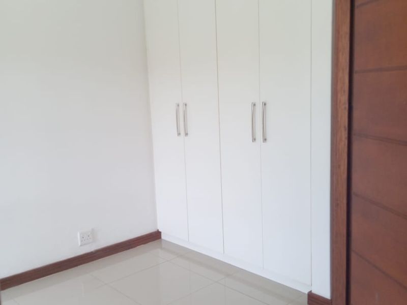 A clean, empty bedroom featuring neutral tiled flooring, white built-in cupboards, and a solid wooden door.