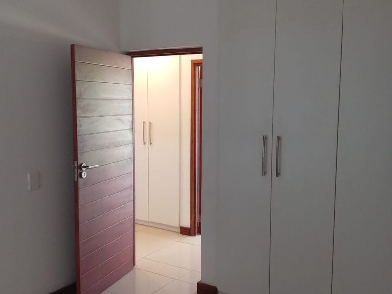 A clean, empty bedroom featuring neutral tiled flooring, white built-in cupboards, and modern internal doors, offering a bright and well-maintained living space.