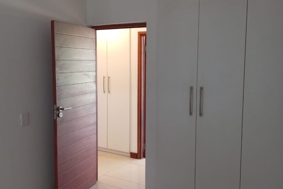 A clean, empty bedroom featuring neutral tiled flooring, white built-in cupboards, and modern internal doors, offering a bright and well-maintained living space.