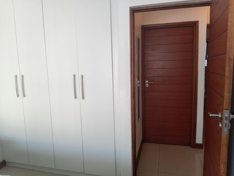 A bedroom interior featuring white built-in cupboards and a wooden door leading to an adjacent space with tiled flooring.