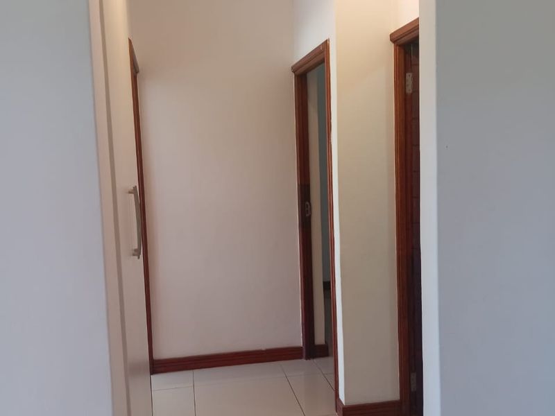 A clean, well-maintained hallway featuring neutral tiled flooring, built-in storage cupboards, and modern spotlight lighting.