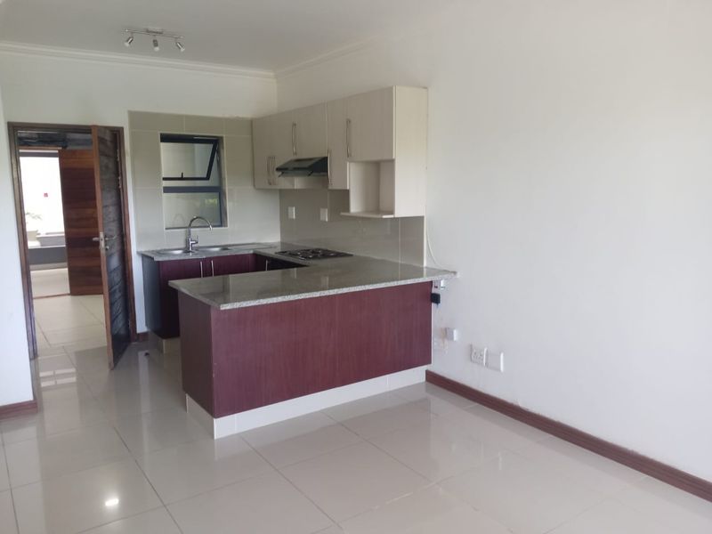 An open-plan kitchen featuring granite countertops, built-in cabinetry, a hob, and an extractor fan, set within a clean, tiled living space.