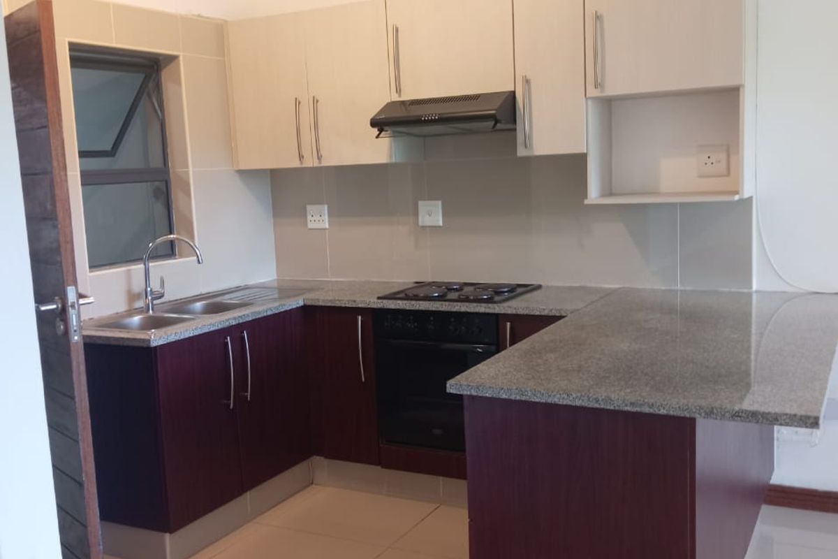A clean, modern kitchen featuring granite countertops, built-in oven, gas hob, extractor fan, and ample cabinetry, finished with neutral tiled flooring.