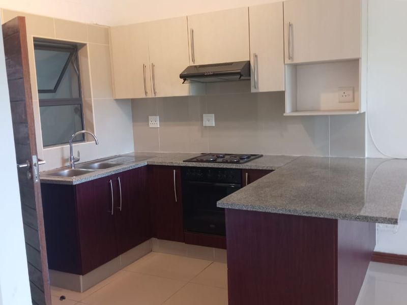 A clean, modern kitchen featuring granite countertops, built-in oven, gas hob, extractor fan, and ample cabinetry, finished with neutral tiled flooring.