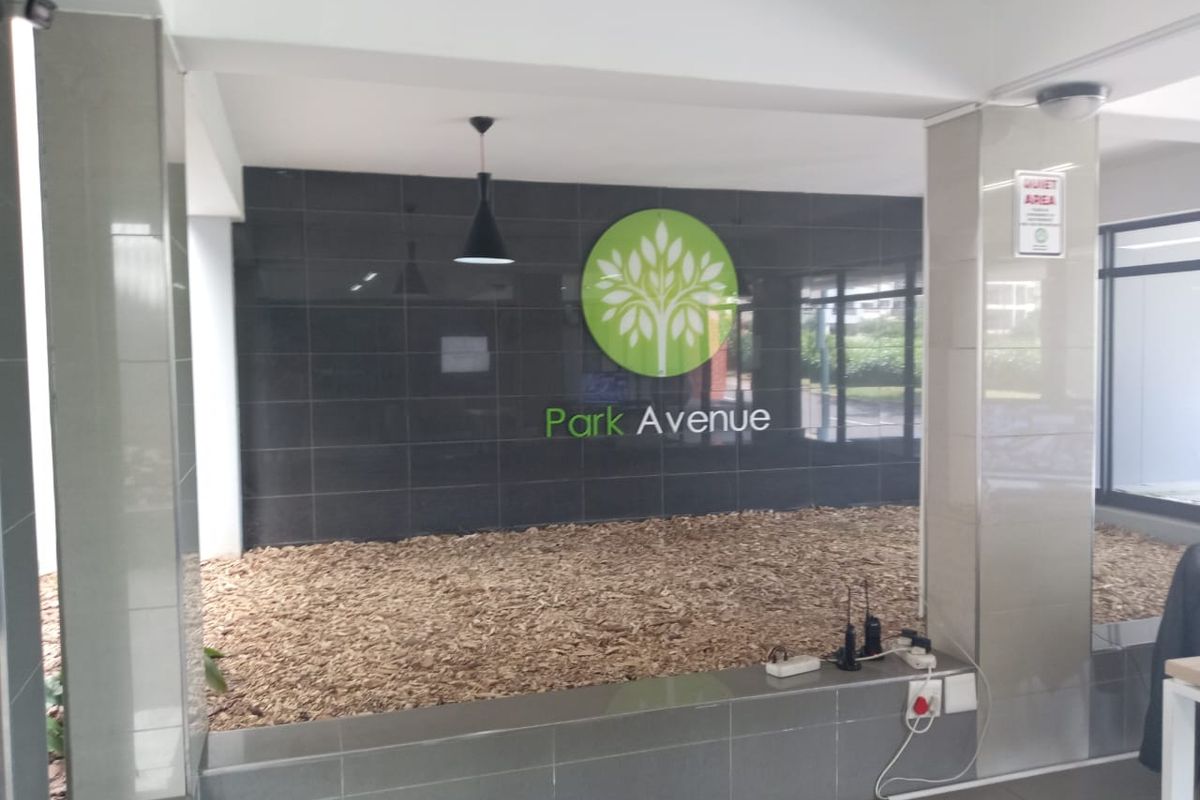 A clean and modern apartment building entrance lobby featuring a tiled feature wall with Park Avenue signage and decorative wood chip landscaping.