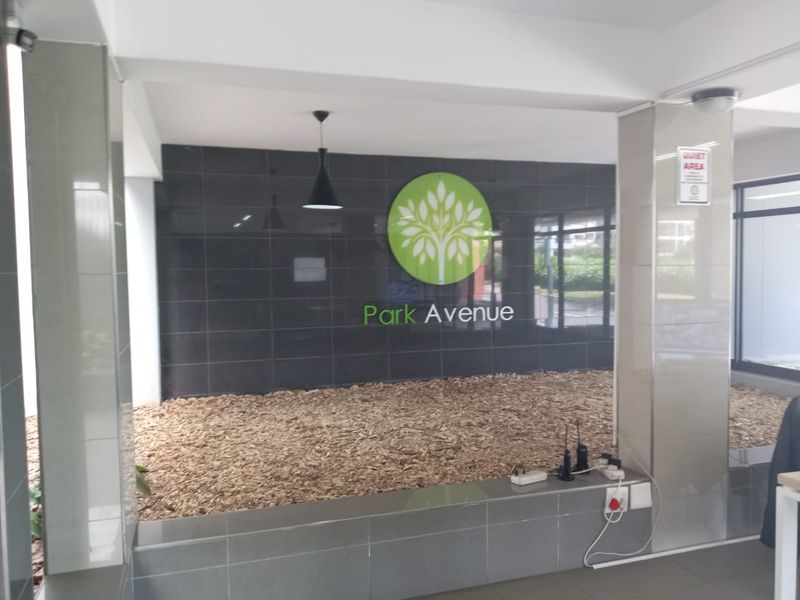 A clean and modern apartment building entrance lobby featuring a tiled feature wall with Park Avenue signage and decorative wood chip landscaping.