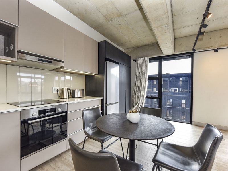 Modern open-plan kitchen featuring sleek cabinetry, integrated appliances, and an exposed concrete ceiling, seamlessly flowing into a dining area with large windows.