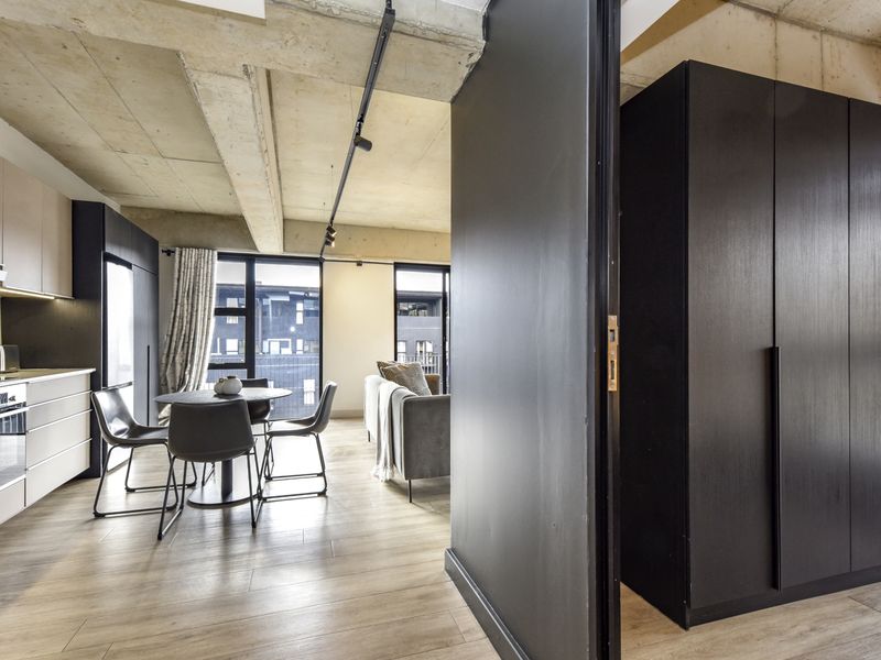 Modern open-plan apartment featuring an industrial-style exposed concrete ceiling, sleek kitchen cabinetry with integrated appliances, and high-quality wood-look flooring.
