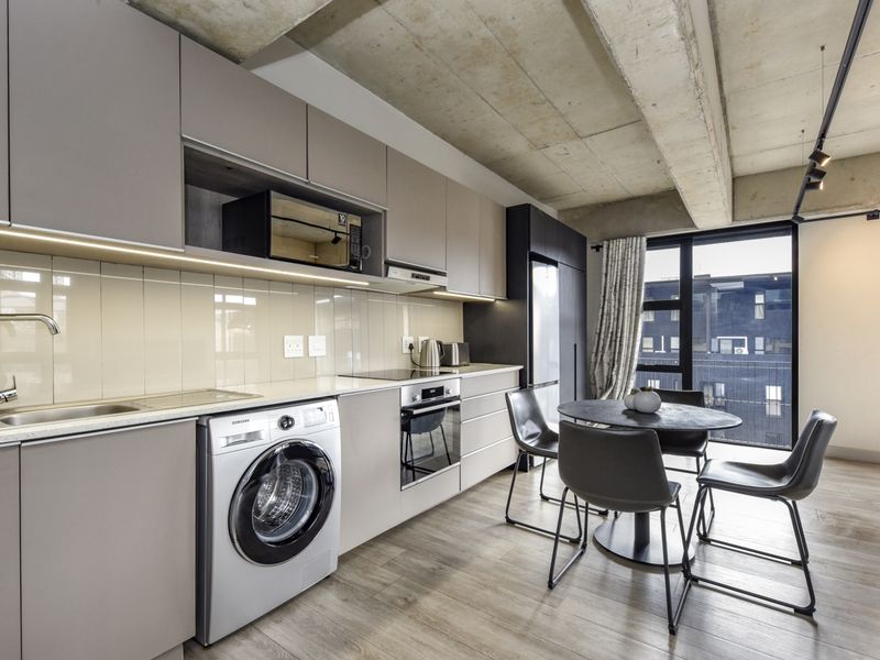 Modern open-plan kitchen and dining area featuring sleek cabinetry, integrated appliances, and an industrial-style exposed concrete ceiling with large windows.